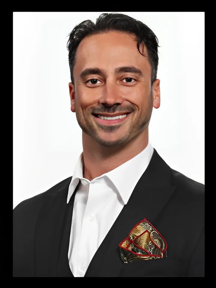 Smiling man in white shirt and black suit with a decorative patterned pocket square.